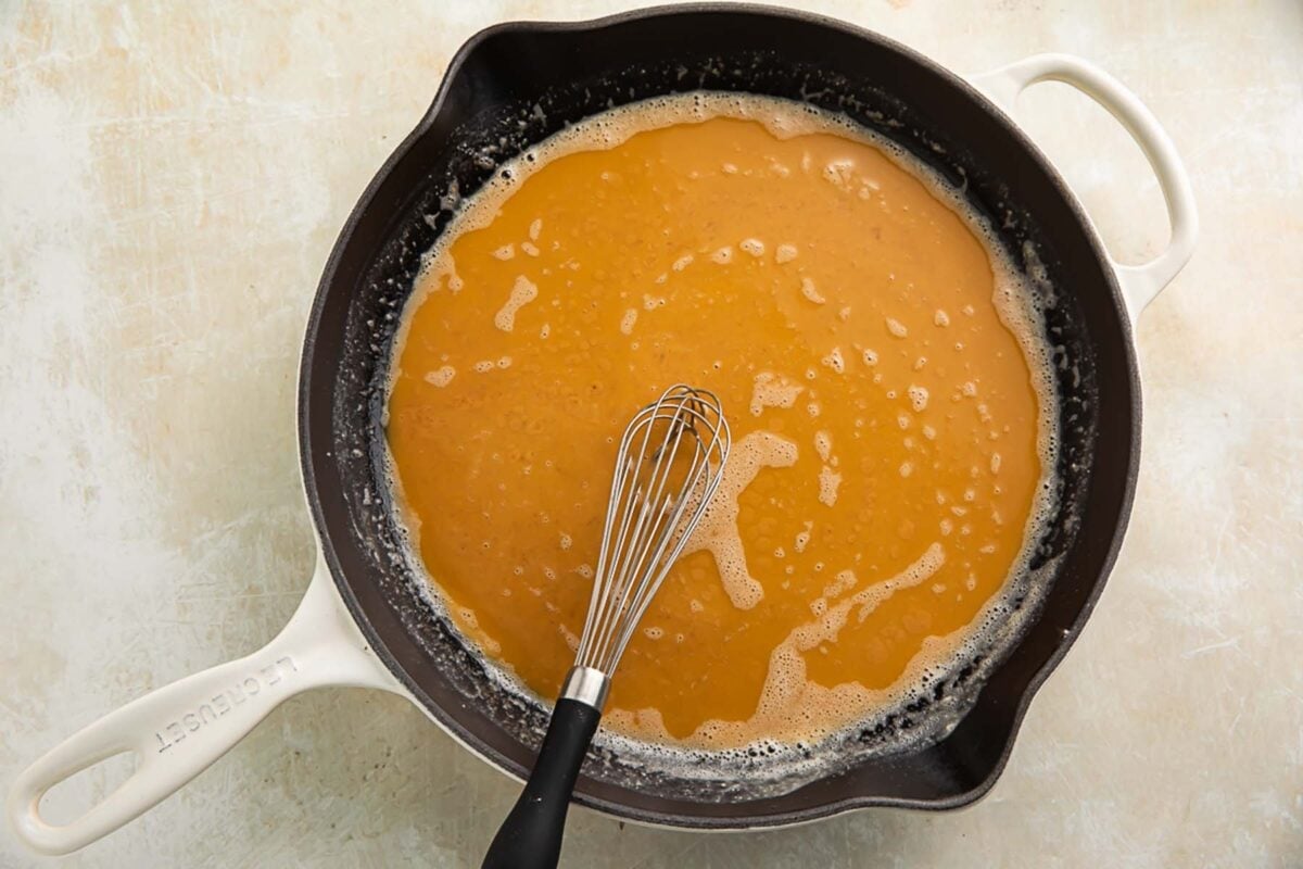 A rich, peanut-buttery roux in a large skillet with a whisk.