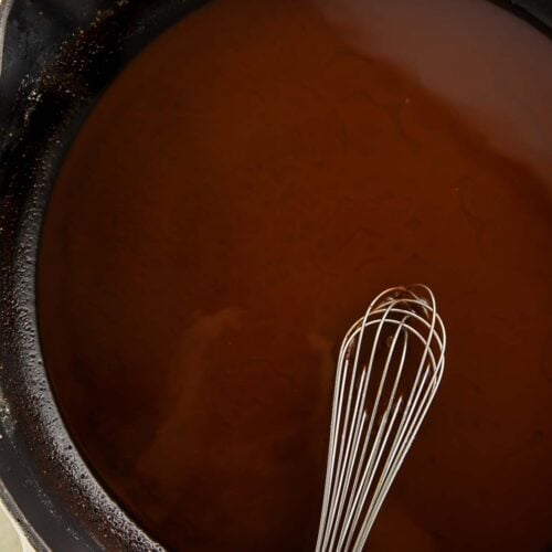 A rich, dark brown Cajun gumbo roux in a large skillet with a whisk.