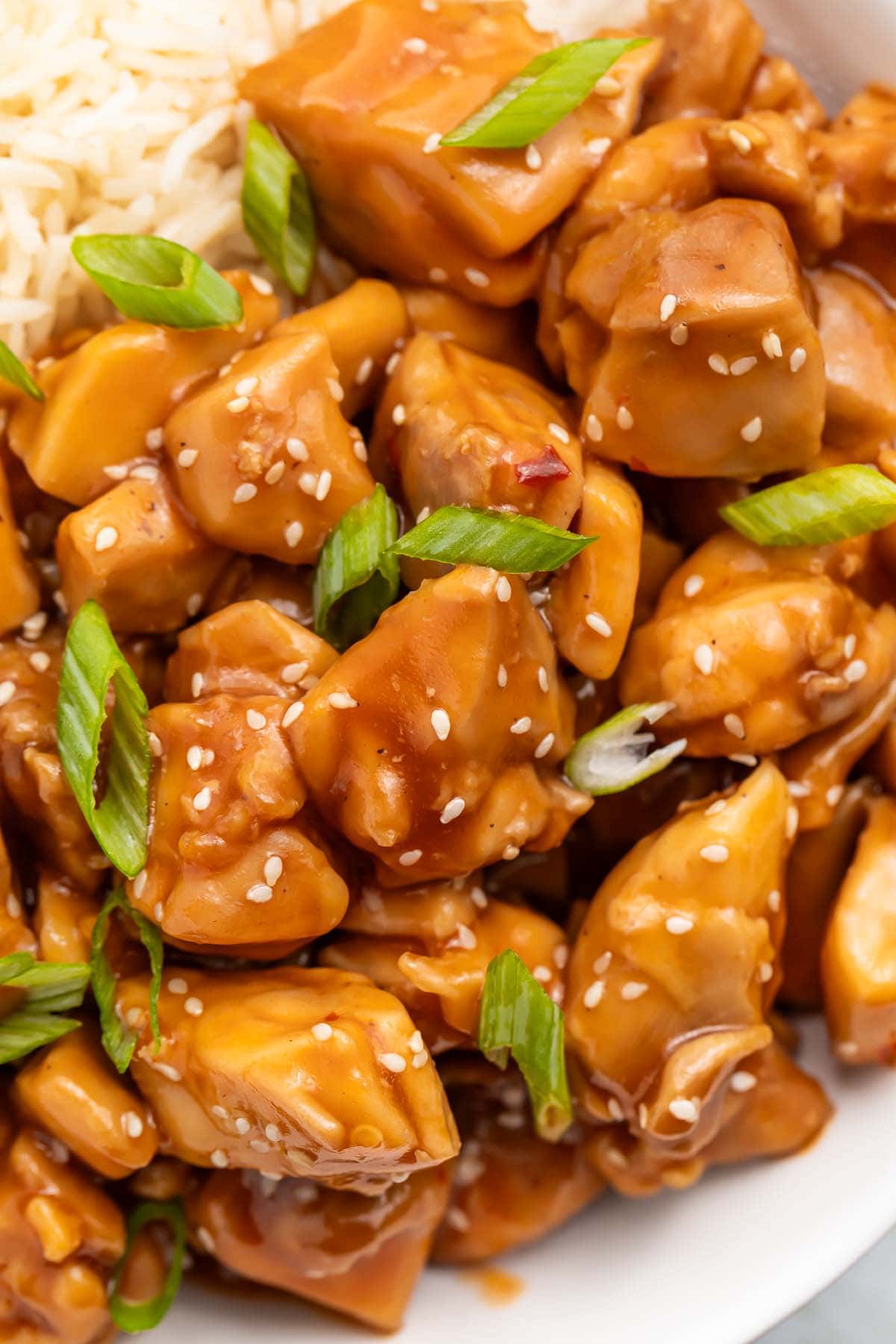 Close-up of a bowl of Instant Pot bourbon chicken with white rice garnished with sliced green onions.