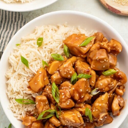 Overhead photo of a bowl of Instant Pot bourbon chicken with white rice garnished with sliced green onions.