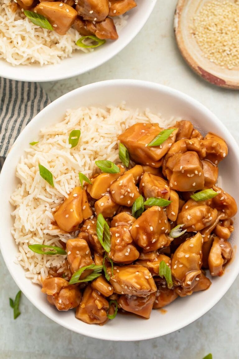 Overhead photo of a bowl of Instant Pot bourbon chicken with white rice garnished with sliced green onions.