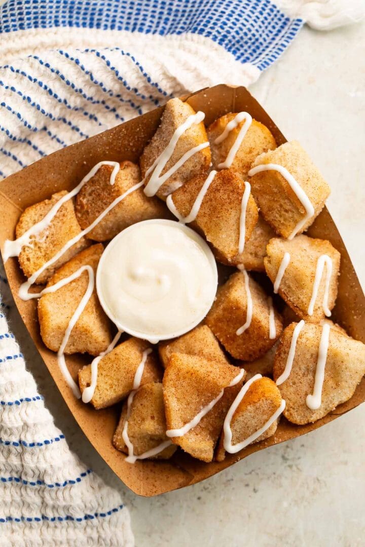 Overhead look at a cardboard tray holding keto cinnamon roll bites (made from keto buns) with a cream cheese icing.