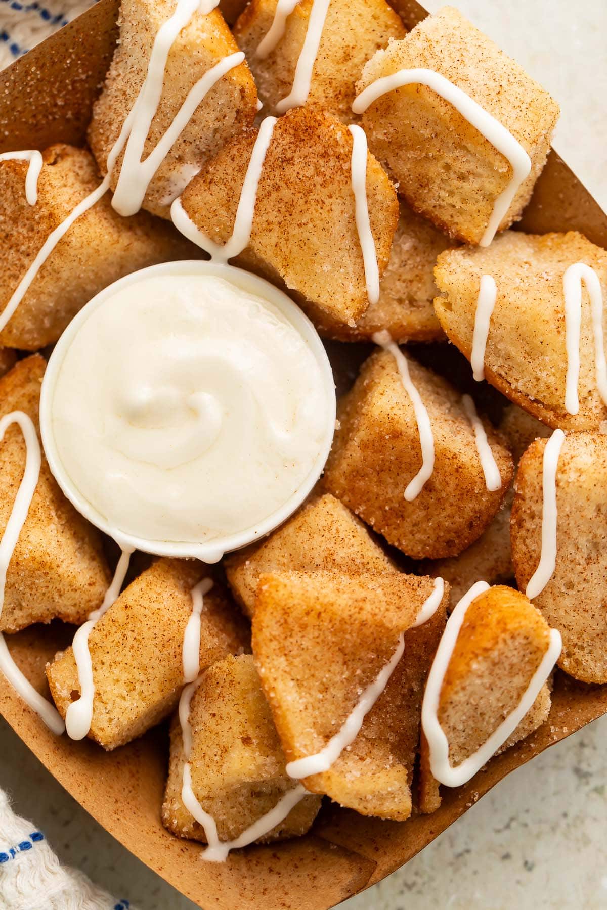 Close-up of a cardboard tray holding keto cinnamon roll bites (made from keto buns) with a cream cheese icing.