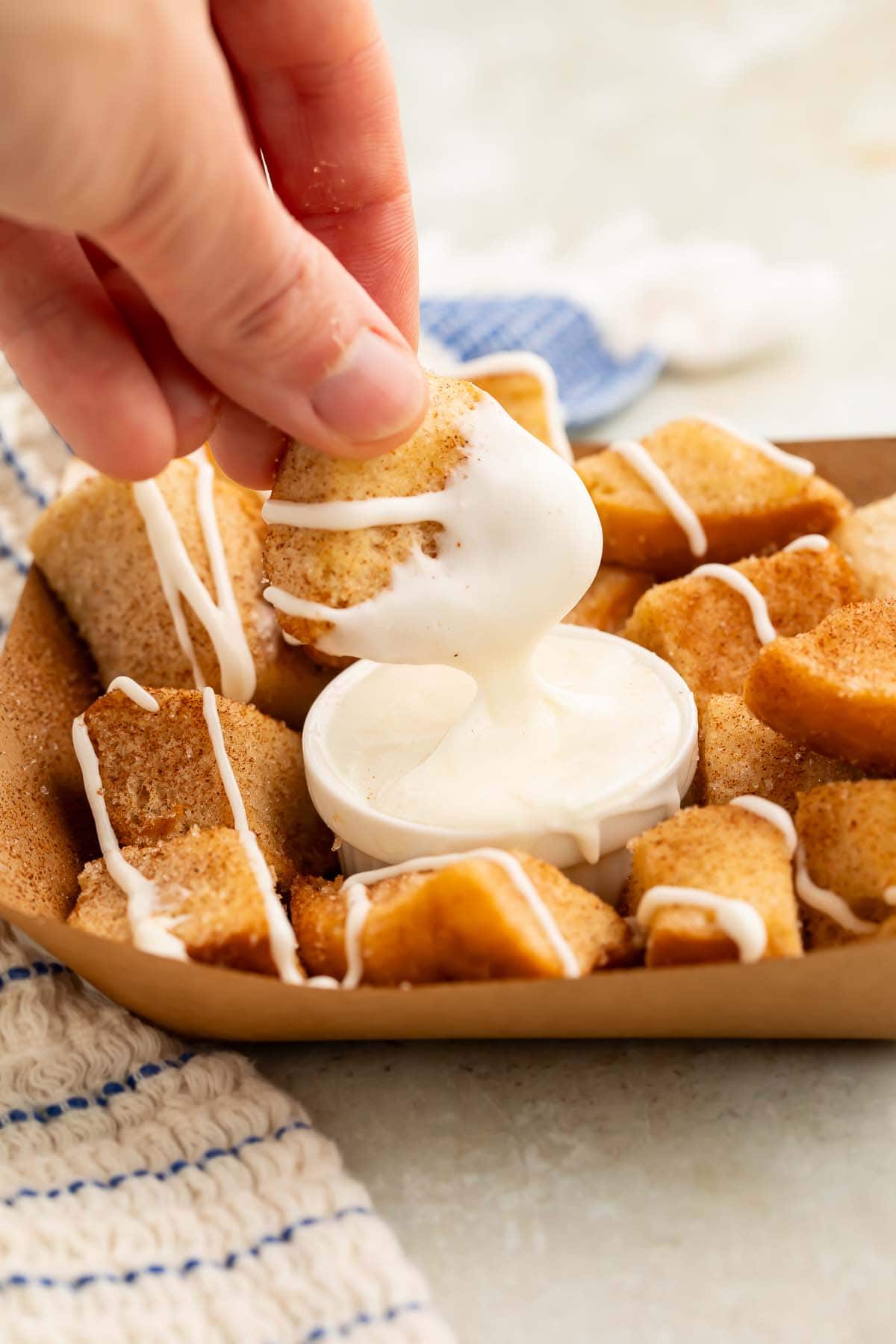 A white woman's hand holding one of the keto cinnamon roll bites, dipping into into a small ramekin of cream cheese icing.