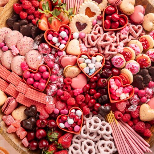 A Valentine's Day themed charcuterie board filled with pink, red, and white cookies, candies, pretzels, fruits, and chocolates.