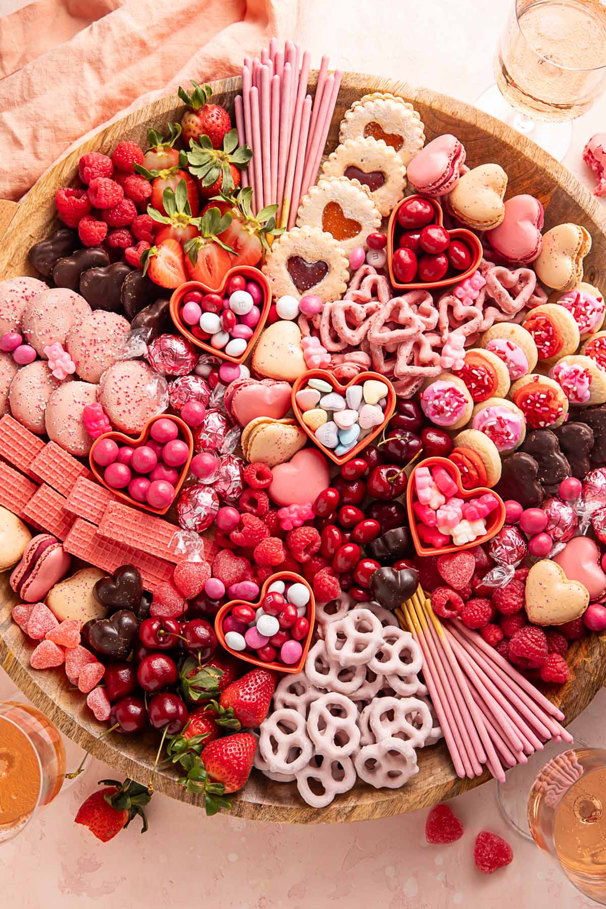 A Valentine's Day themed charcuterie board filled with pink, red, and white cookies, candies, pretzels, fruits, and chocolates.