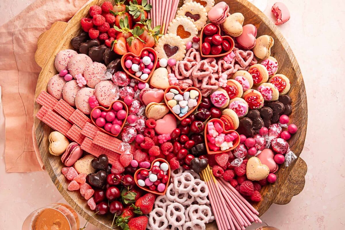 A Valentine's Day themed charcuterie board filled with pink, red, and white cookies, candies, pretzels, fruits, and chocolates.