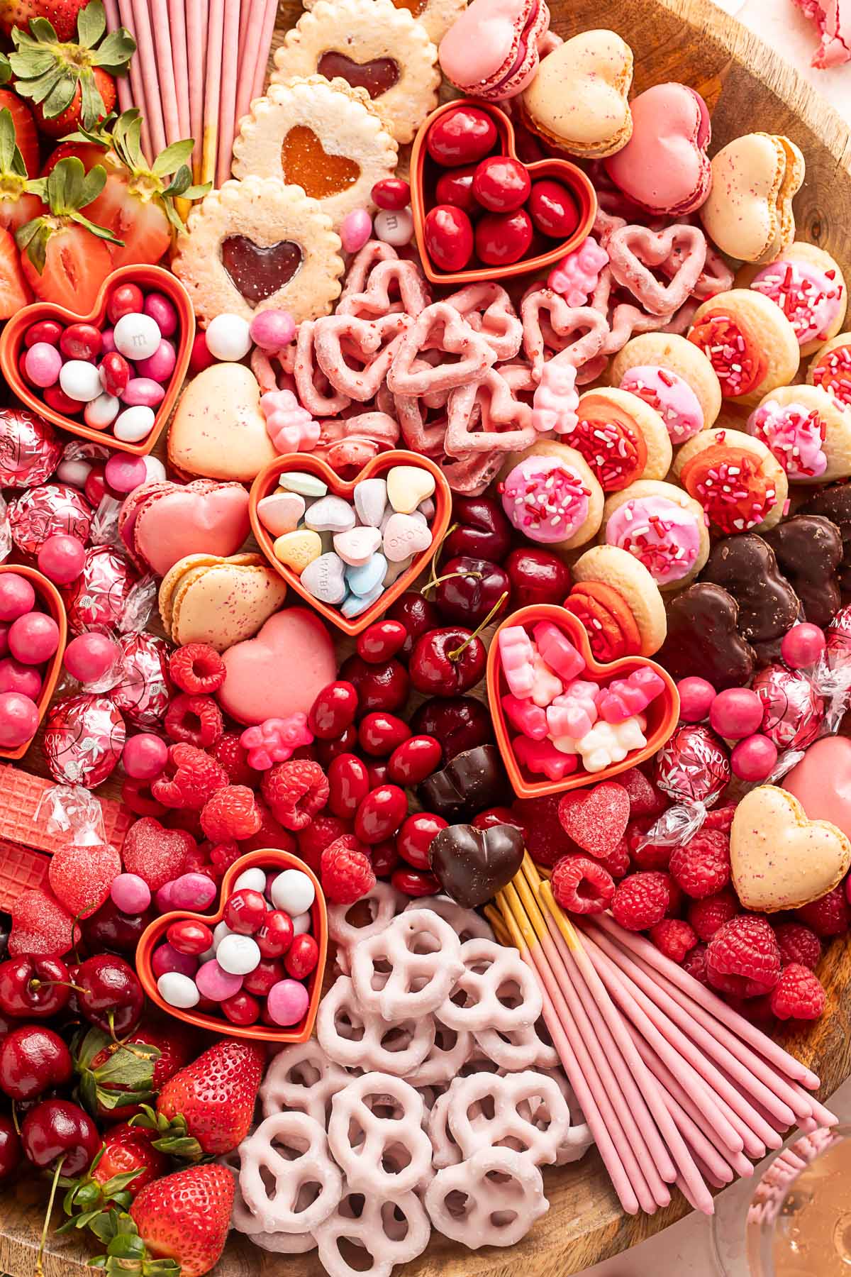 A Valentine's Day themed charcuterie board filled with pink, red, and white cookies, candies, pretzels, fruits, and chocolates.