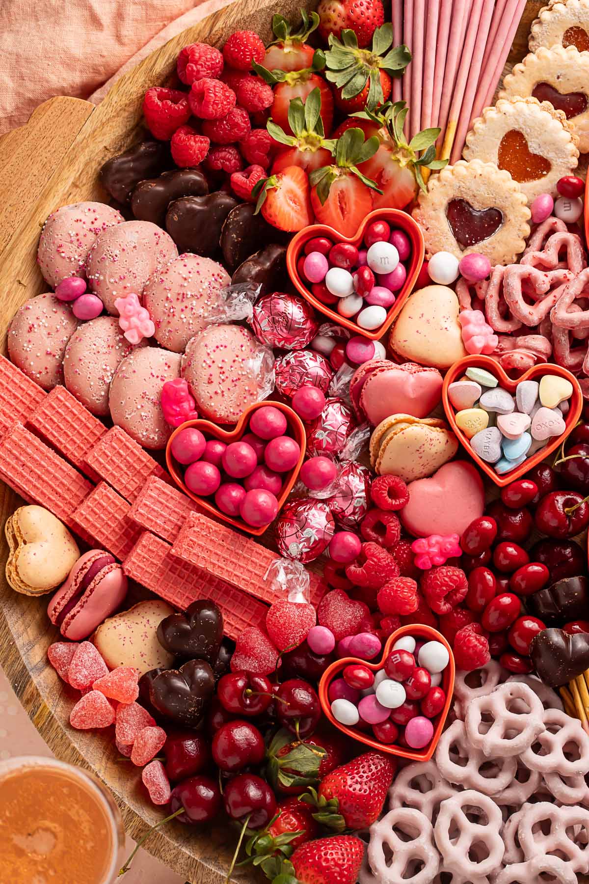 A Valentine's Day themed charcuterie board filled with pink, red, and white cookies, candies, pretzels, fruits, and chocolates.