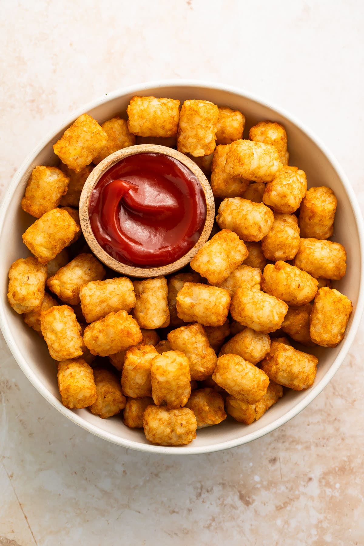Overhead photo of a large bowl of air fryer tater tots with a ramekin of deep red ketchup.
