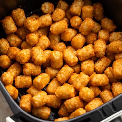 Golden, crispy tater tots in a black air fryer basket.