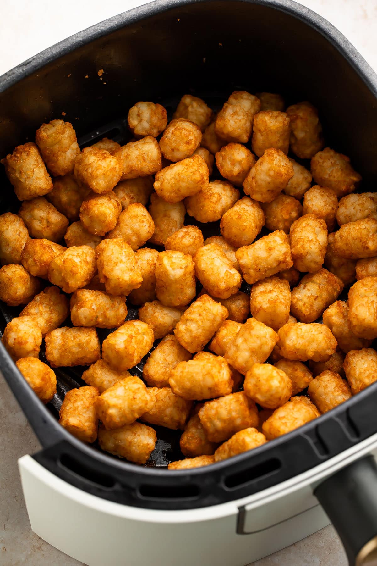 Golden, crispy tater tots in a black air fryer basket.