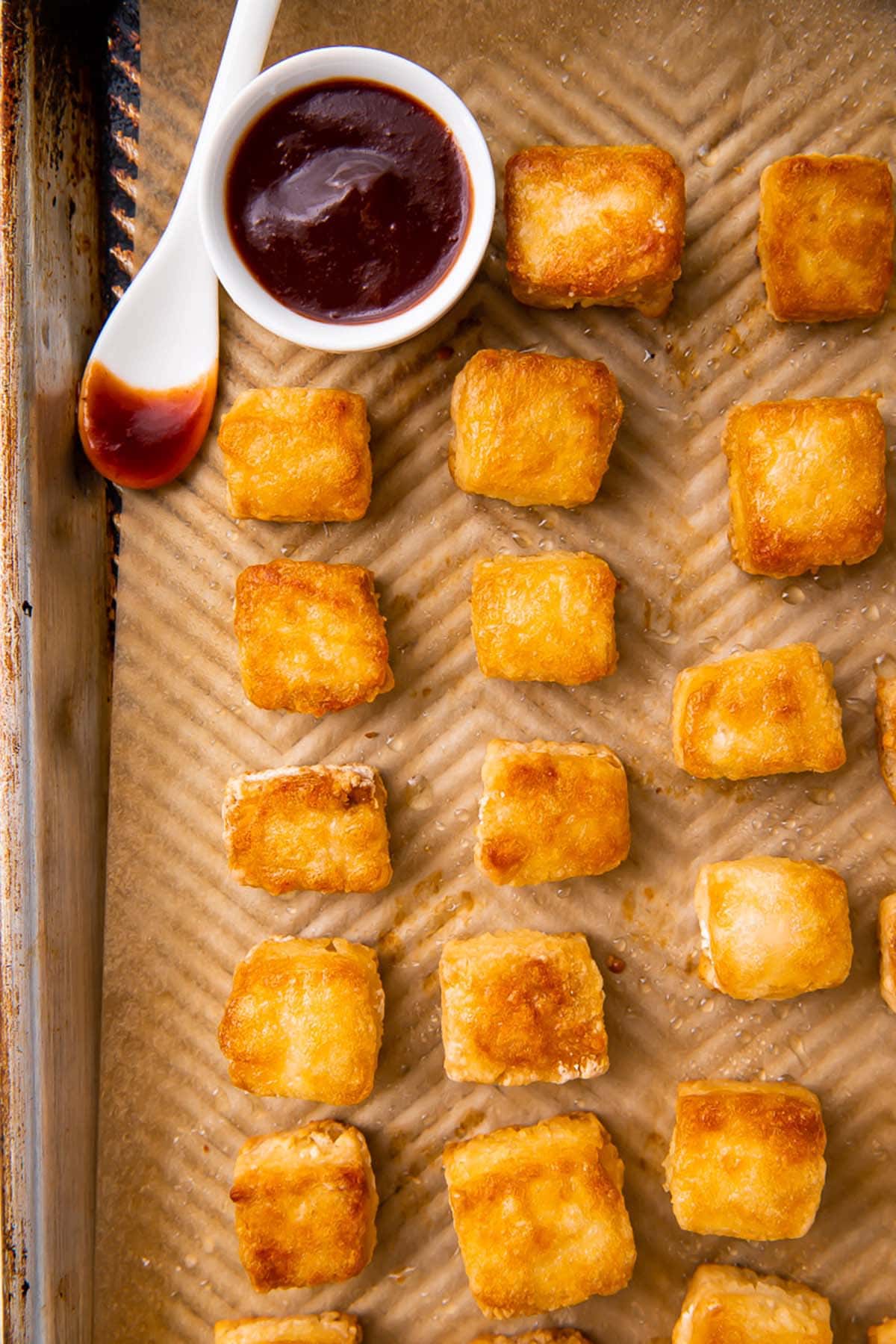 Crispy baked tofu cubes arranged on a baking sheet next to a ramekin of BBQ sauce.