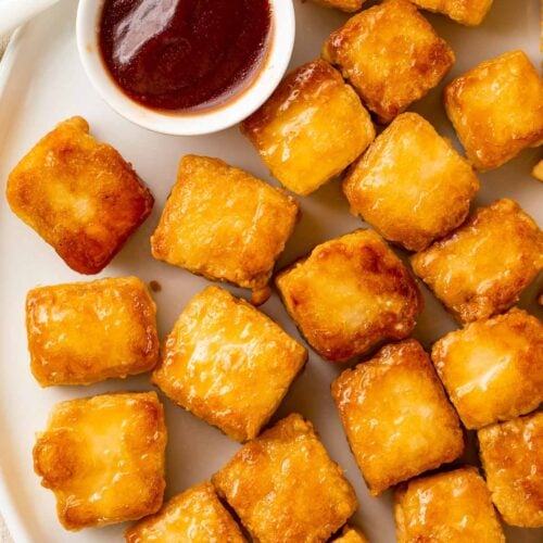 Crispy baked tofu cubes arranged on a plate next to a ramekin of BBQ sauce.