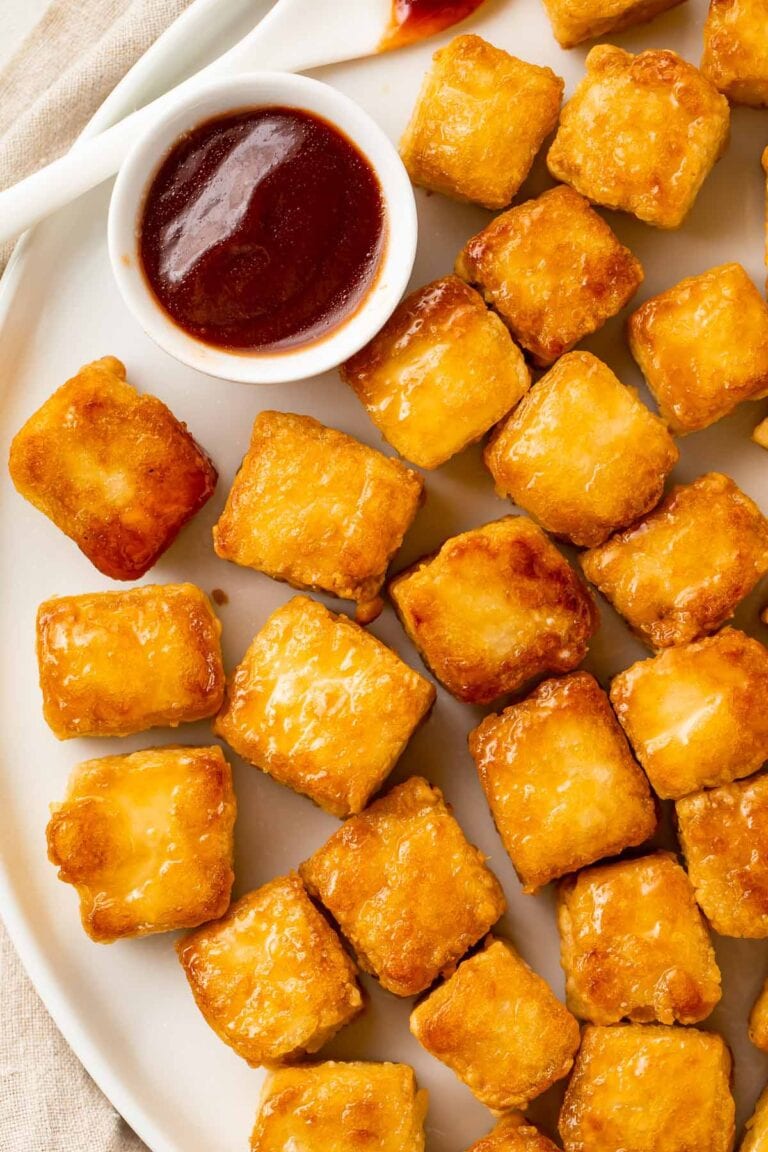 Crispy baked tofu cubes arranged on a plate next to a ramekin of BBQ sauce.