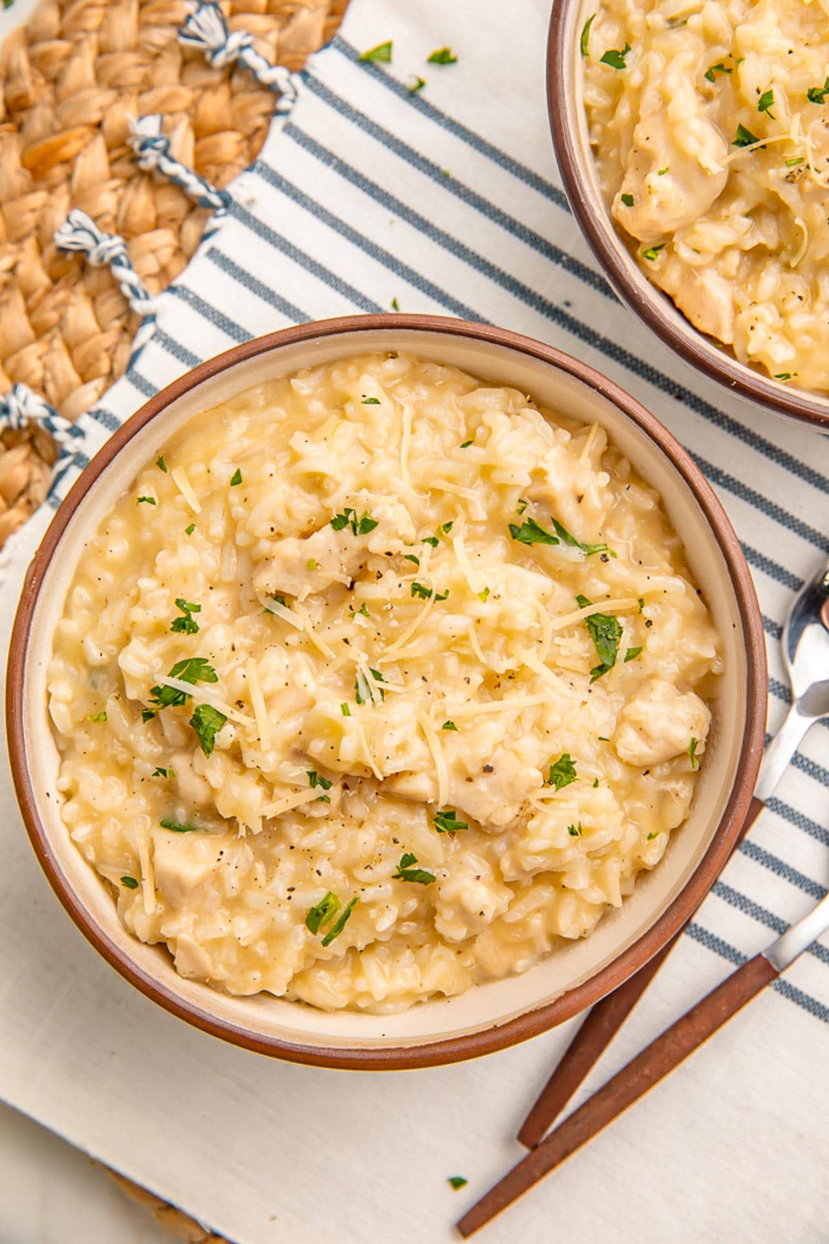 A bowl of creamy Instant Pot chicken and rice sitting on a blue and natural kitchen towel and rattan placemat.