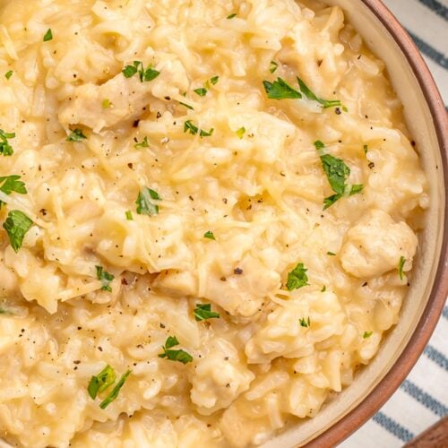 Bowl of creamy Instant Pot chicken and rice with melted Parmesan cheese and fresh parsley on a striped kitchen towel.