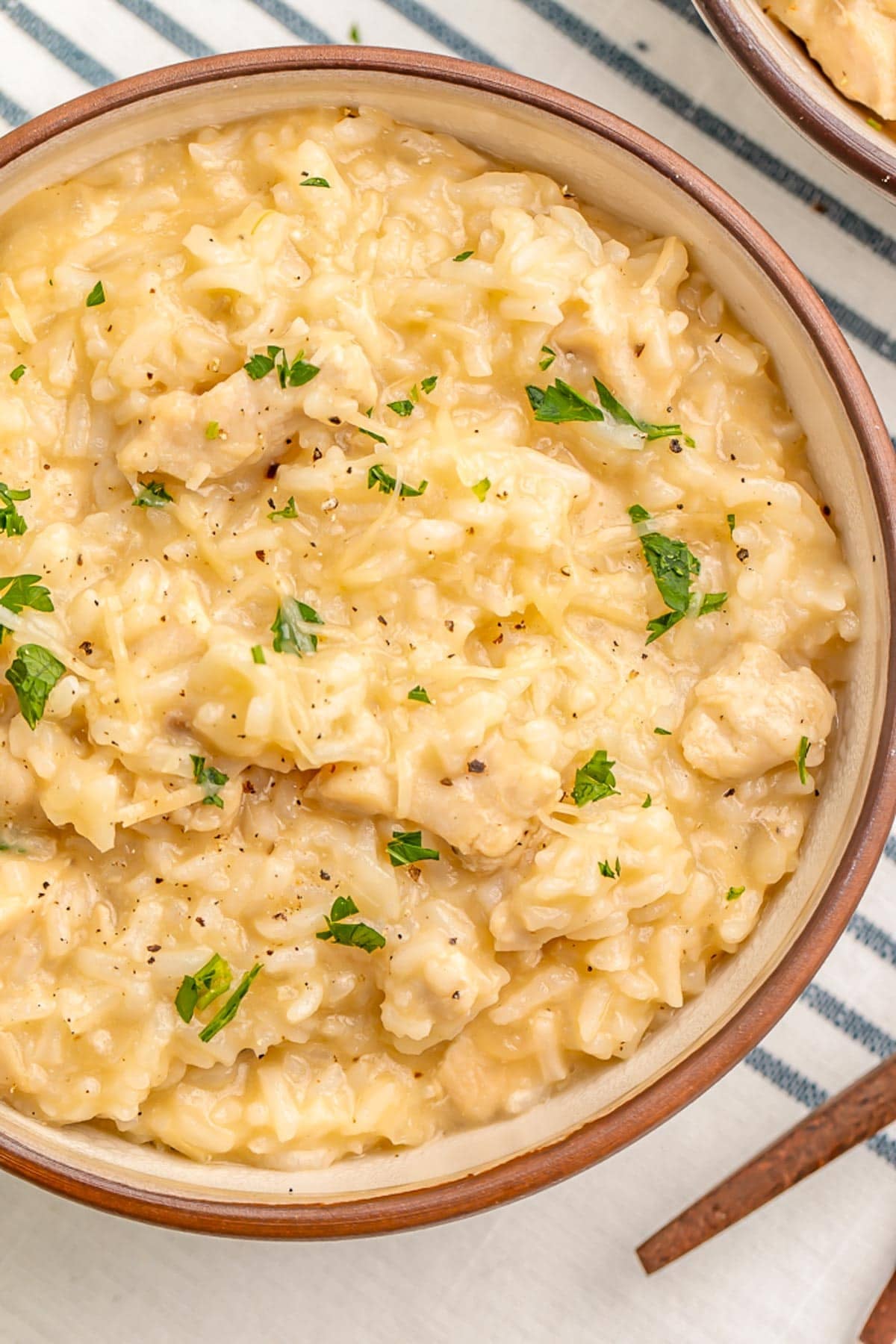 Bowl of creamy Instant Pot chicken and rice with melted Parmesan cheese and fresh parsley on a striped kitchen towel.