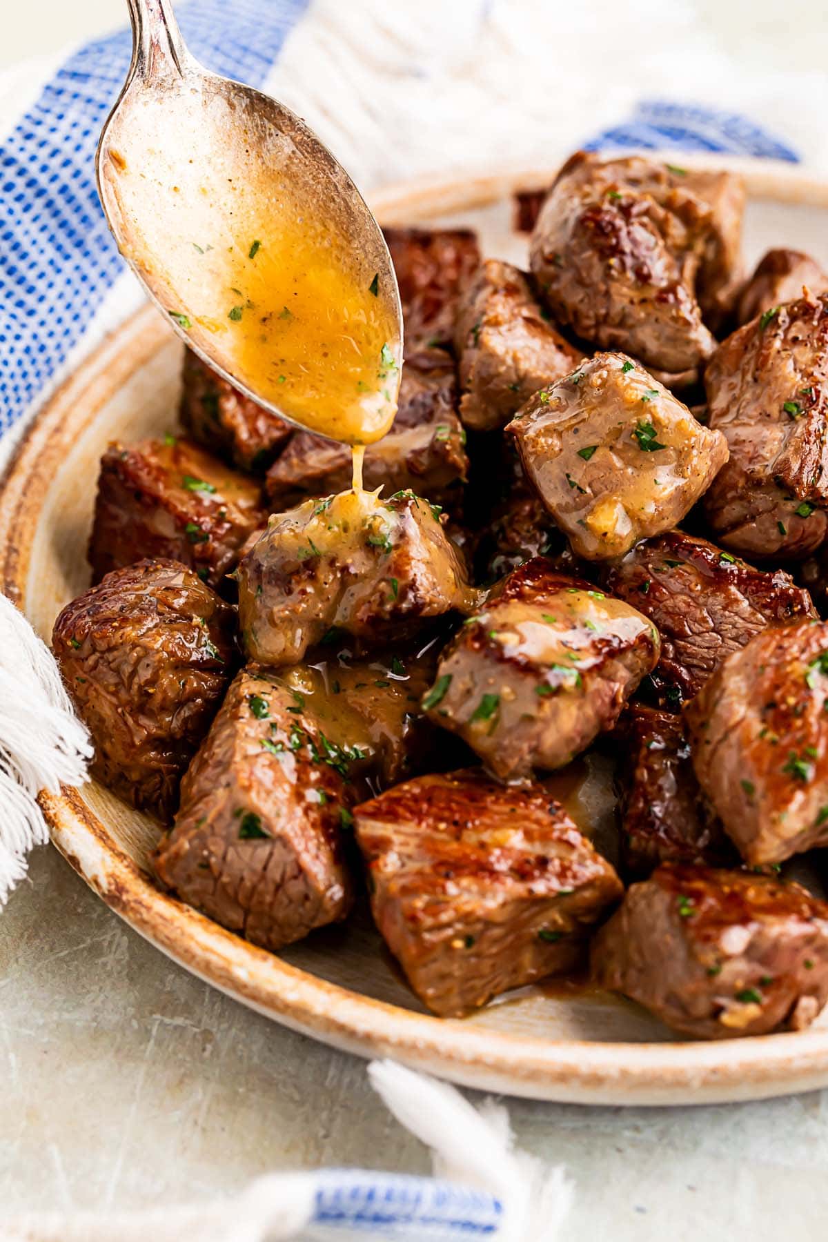 Garlic butter being spooned over steak bites in a large bowl.