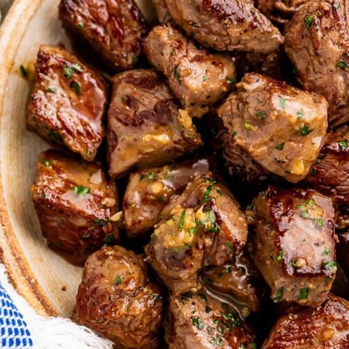 A large bowl of garlic butter steak bites next to a blue and white kitchen towel.