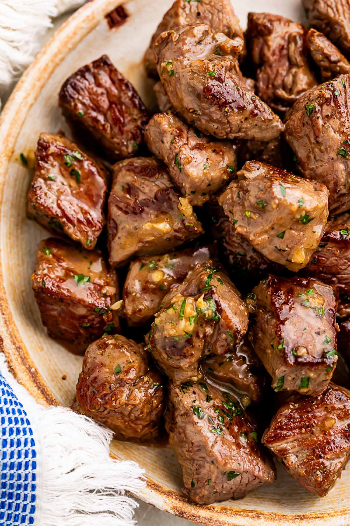 A large bowl of garlic butter steak bites next to a blue and white kitchen towel.