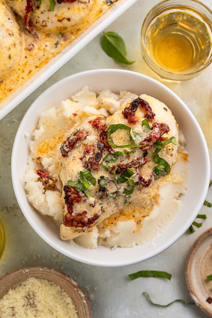 A bowl of creamy marry me chicken casserole on a bed of mashed potatoes.