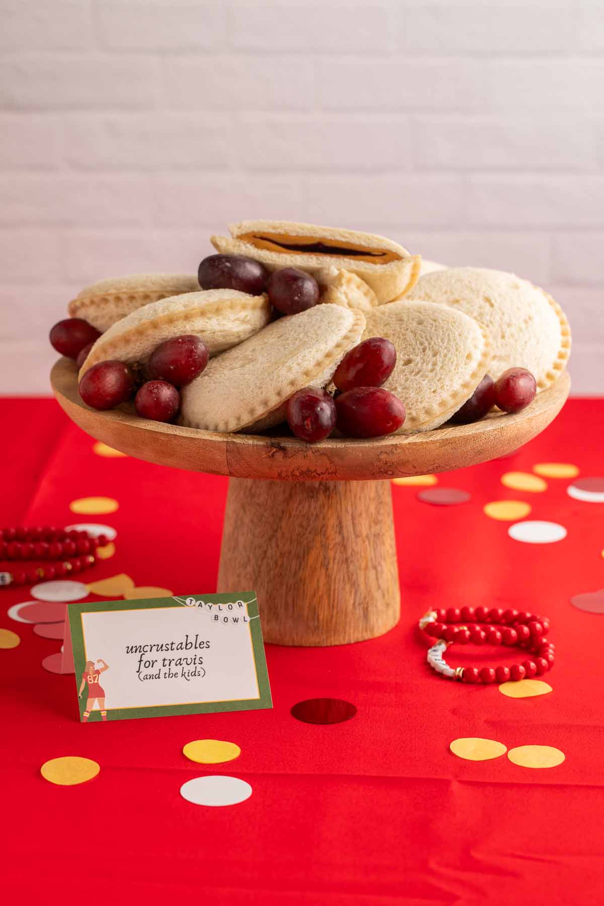 A wooden cake stand holding an arrangement of peanut butter and grape jelly Uncrustables.