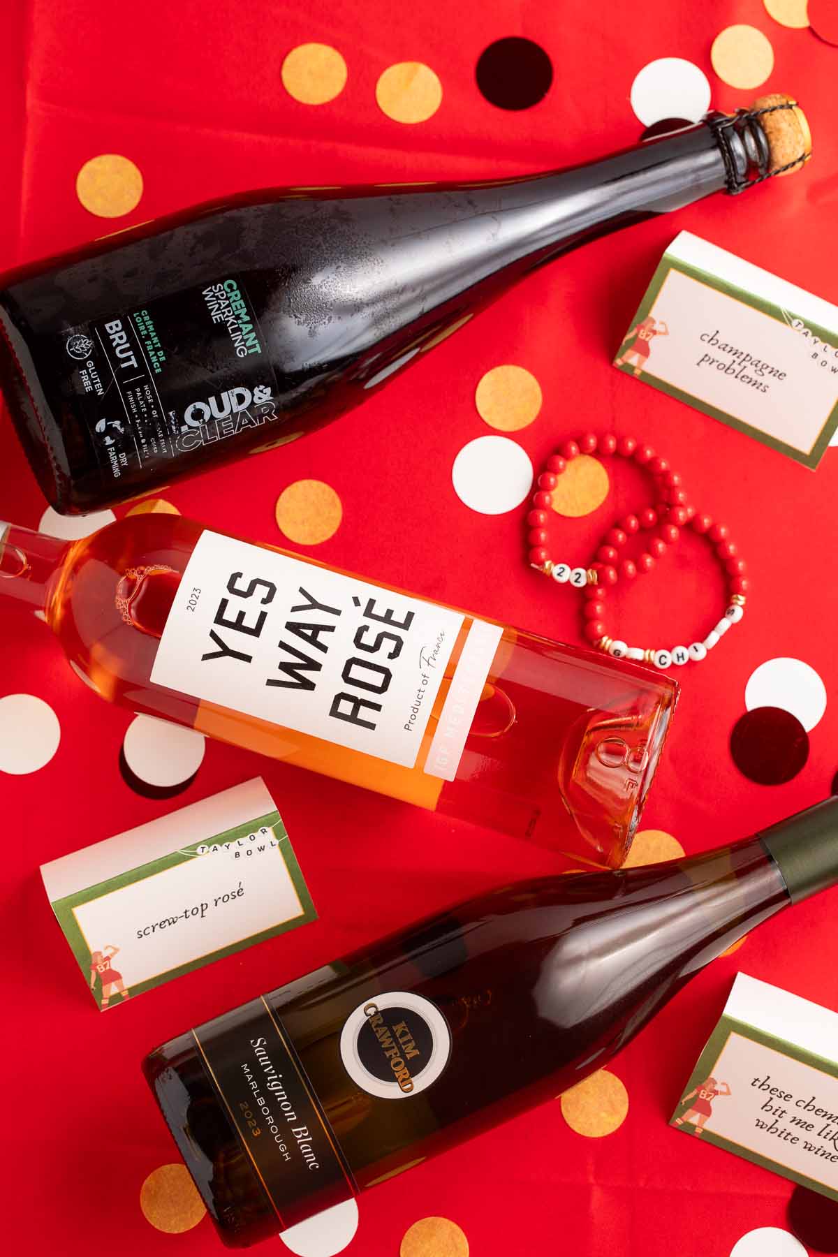 Champagne, white wine, and rosé bottles arrange on a table covered with a red table cloth.