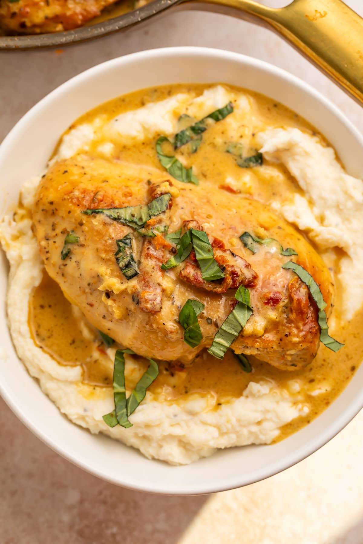 Single Whole30 marry me chicken breast on mashed cauliflower with creamy sauce and basil garnish.