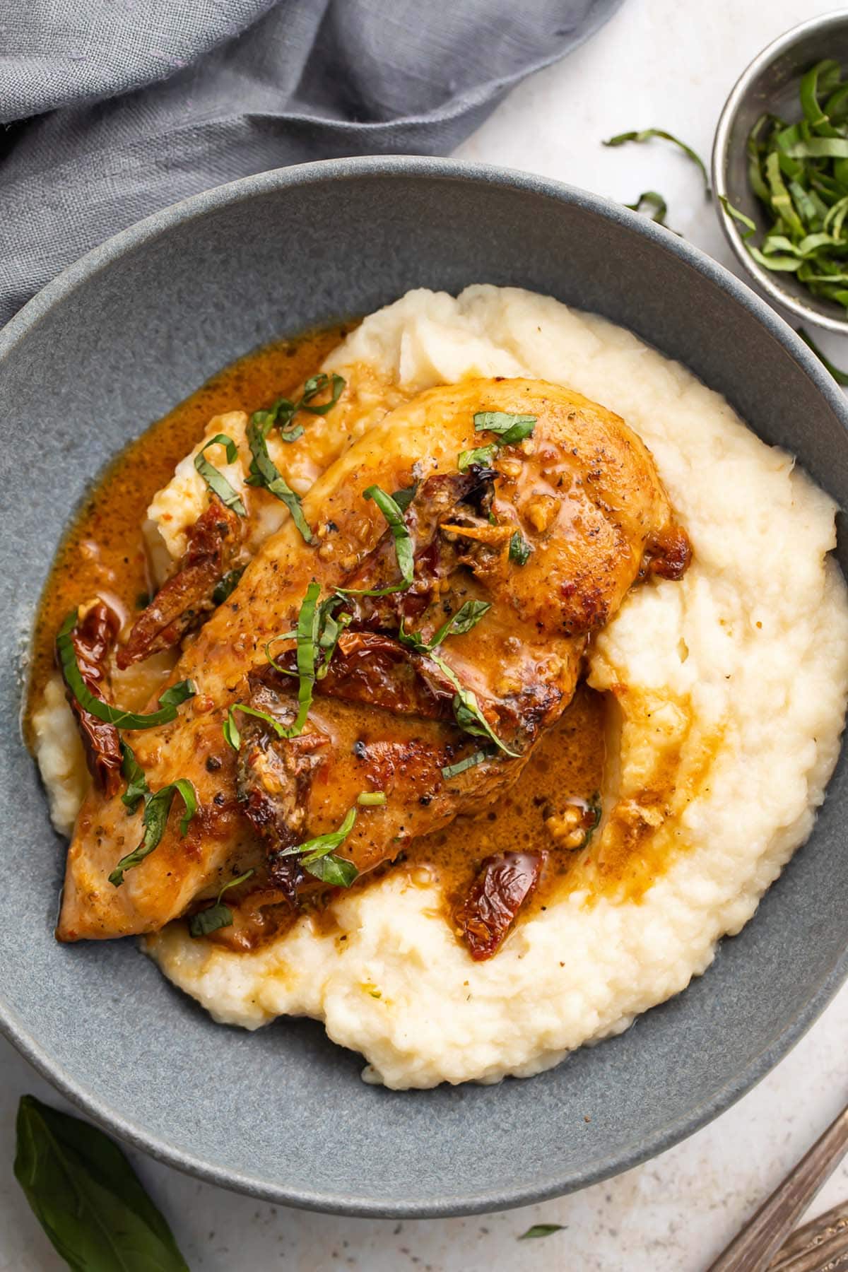 Whole30 marry me chicken on a bed of mashed potatoes in a large shallow blue bowl.