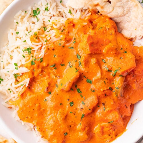 A bowl of chicken tikka masala with rice and a piece of pita bread.