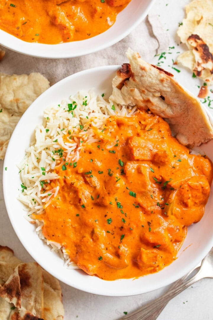 A bowl of chicken tikka masala with rice and a piece of pita bread.