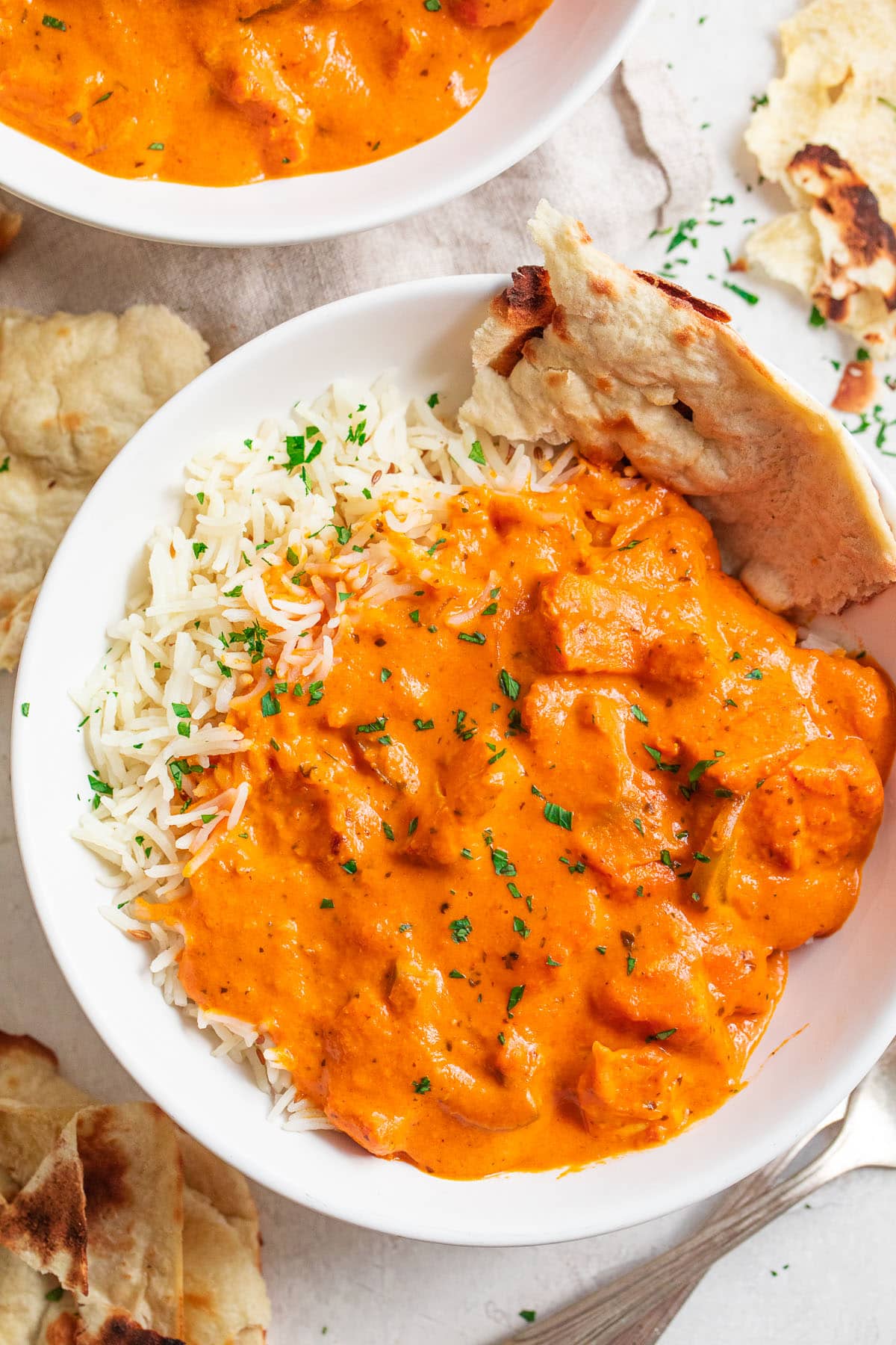 A bowl of chicken tikka masala with rice and a piece of pita bread.