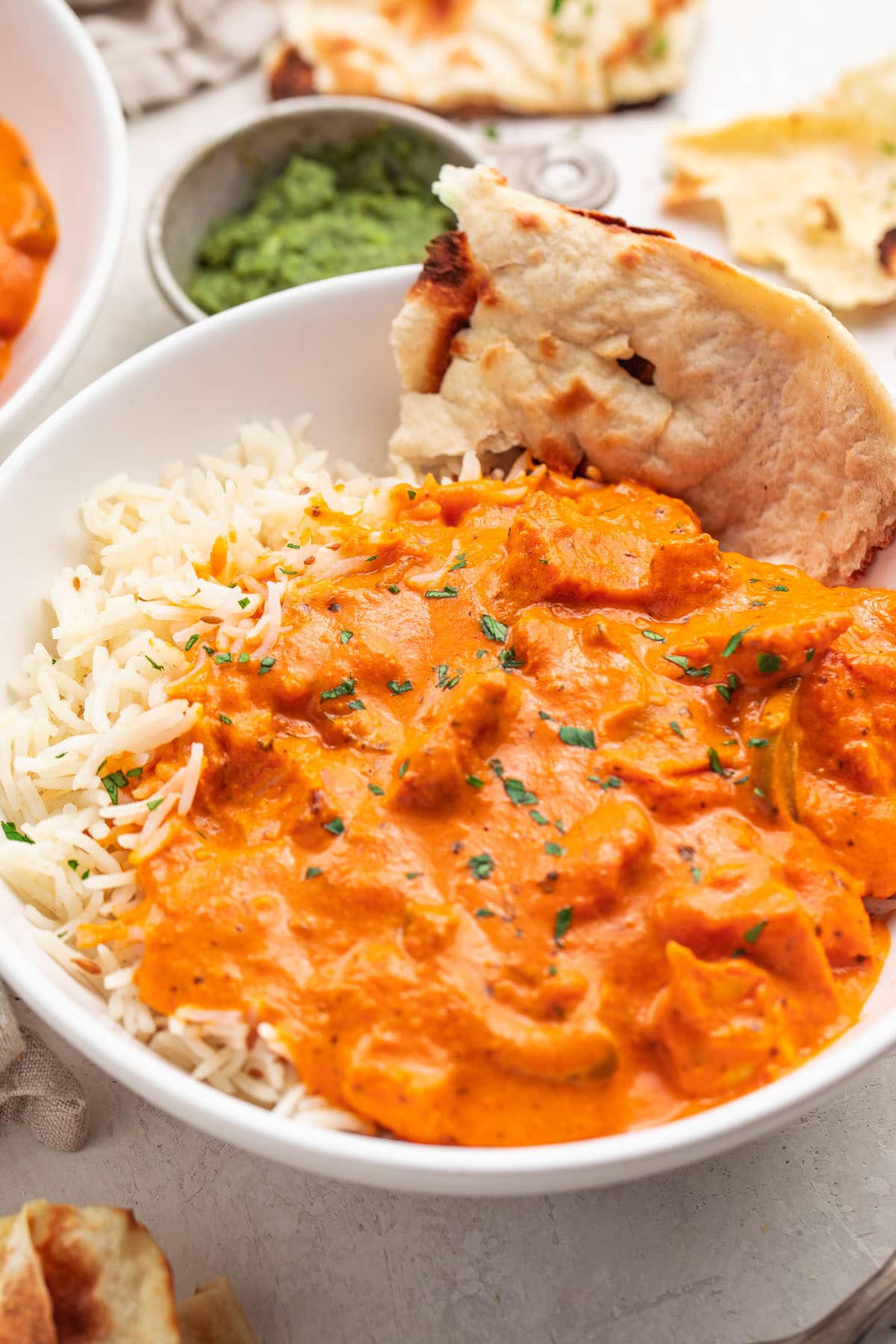 A bowl of chicken tikka masala with rice and a piece of pita bread.