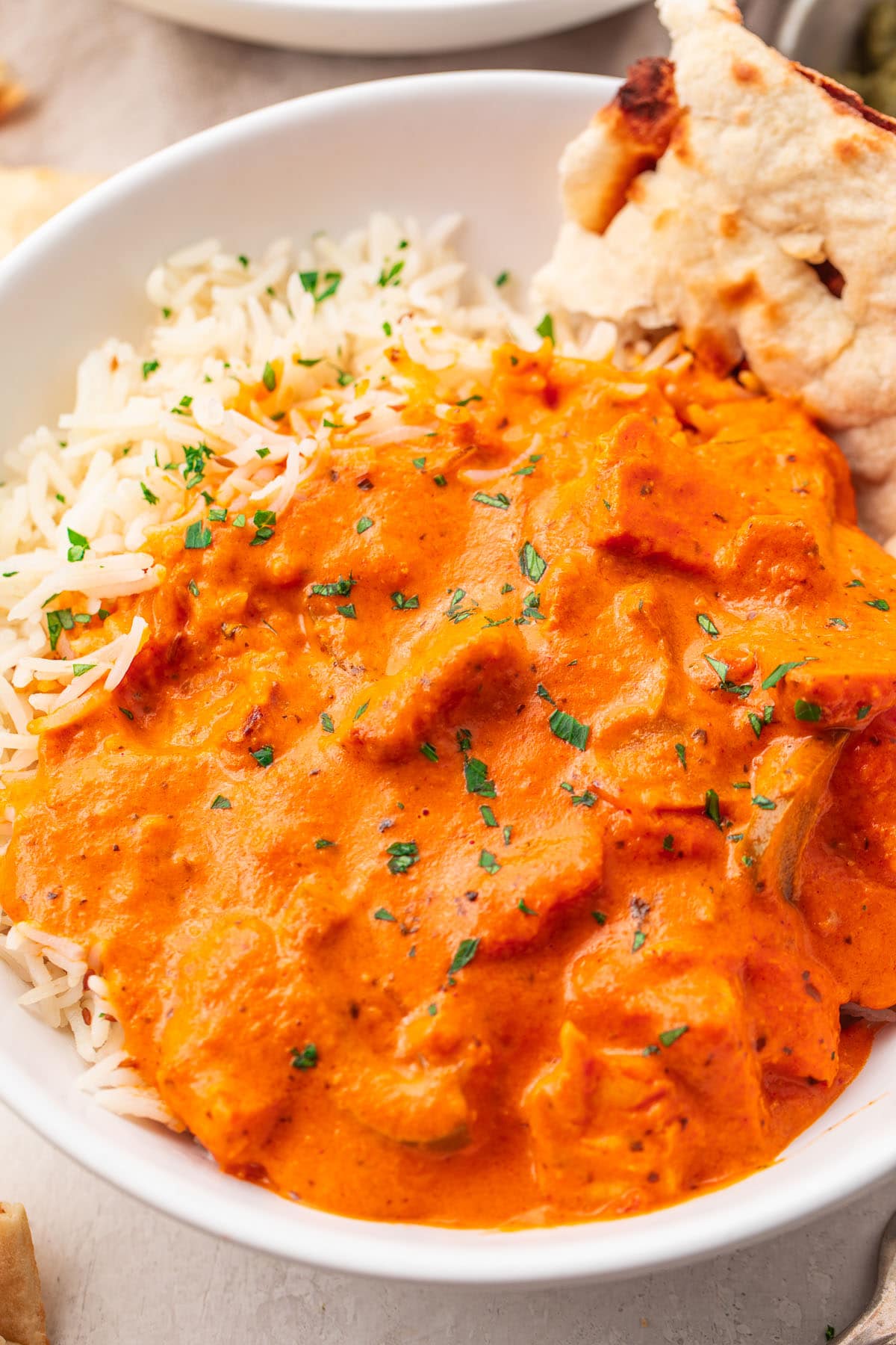 A bowl of chicken tikka masala with rice and a piece of pita bread.