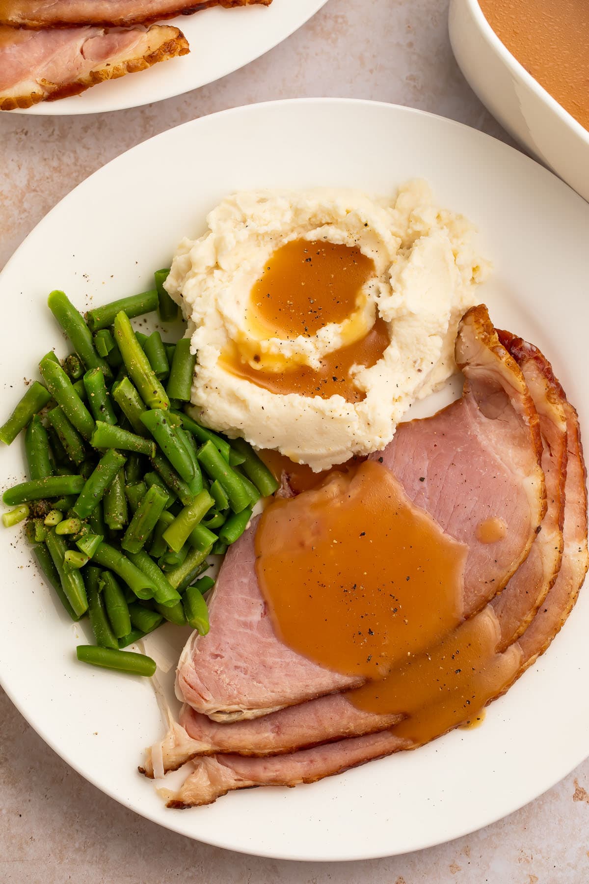 A plate of green beans, mashed potatoes, and slices of ham, topped with creamy brown ham gravy.