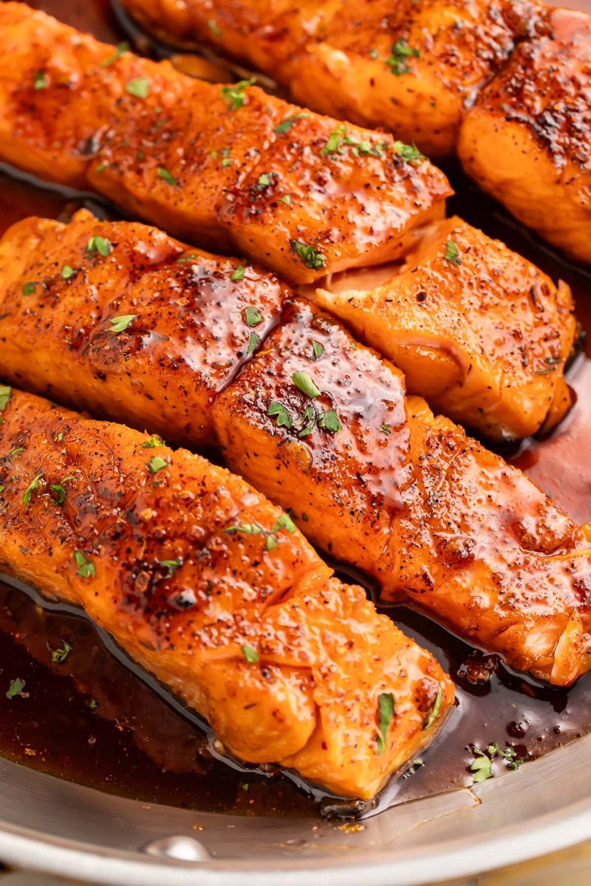 4 salmon fillets smothered in a rich hot honey sauce resting in a large silver skillet.