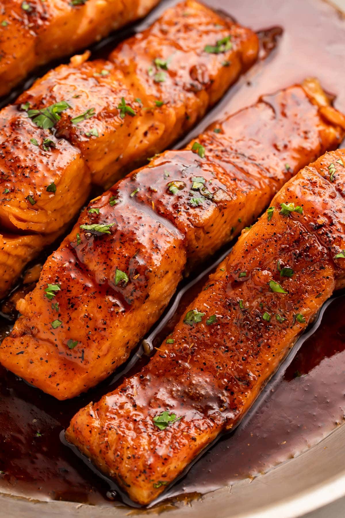 4 salmon fillets smothered in a rich hot honey sauce resting in a large silver skillet.