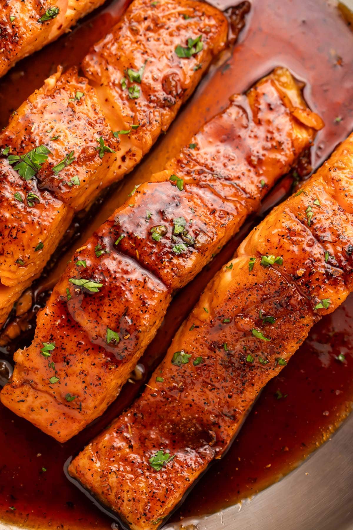 Overhead photo of 4 salmon fillets smothered in a rich hot honey sauce resting in a large silver skillet.