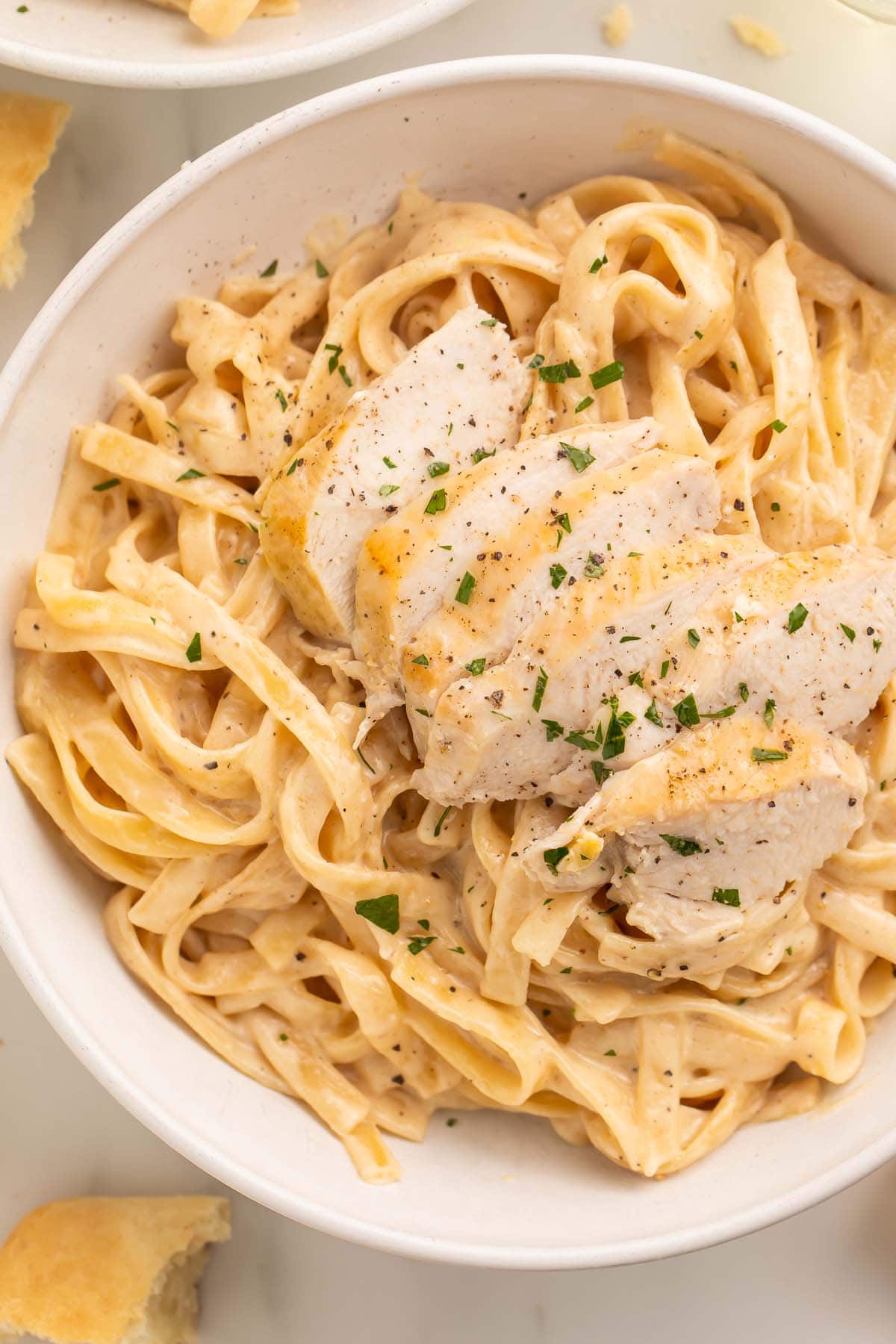 Close-up of Instant Pot chicken alfredo in a large white bowl on a table.