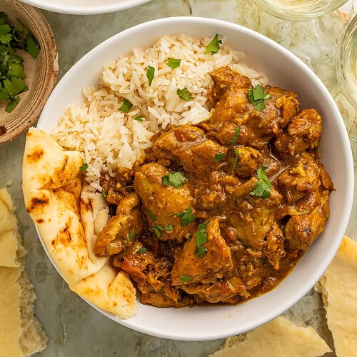 Chicken curry and basmati rice in a white bowl garnished with fresh cilantro leaves