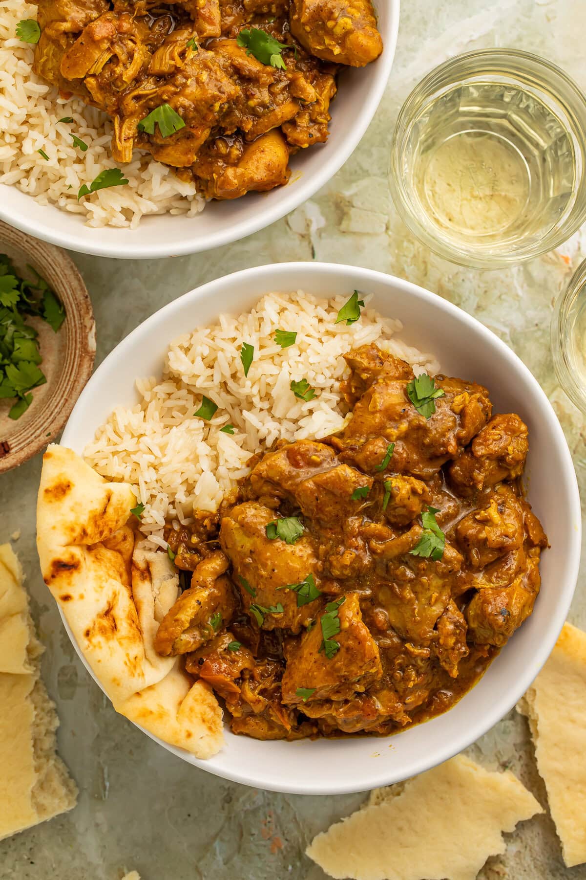 Chicken curry and basmati rice in a white bowl garnished with fresh cilantro leaves
