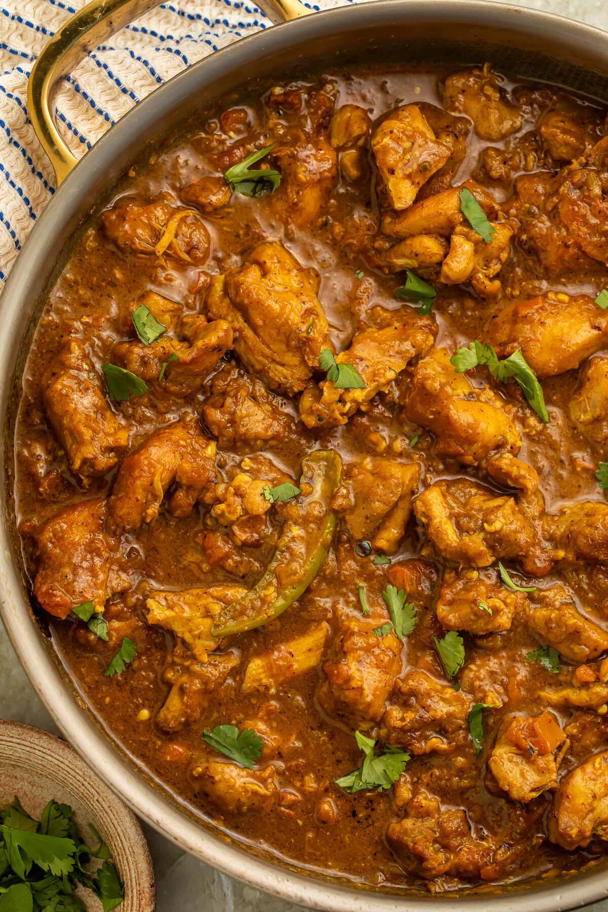 Close-up of glossy restaurant-style chicken curry simmering in a gold pan.