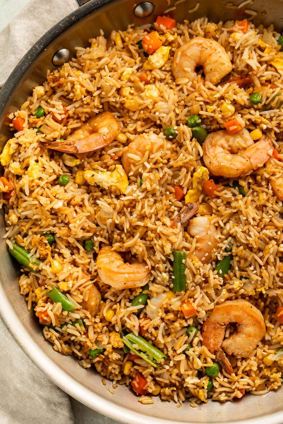 A large silver skillet holding fully-prepared shrimp fried rice with large juicy shrimp, green beans, and peas littered throughout.