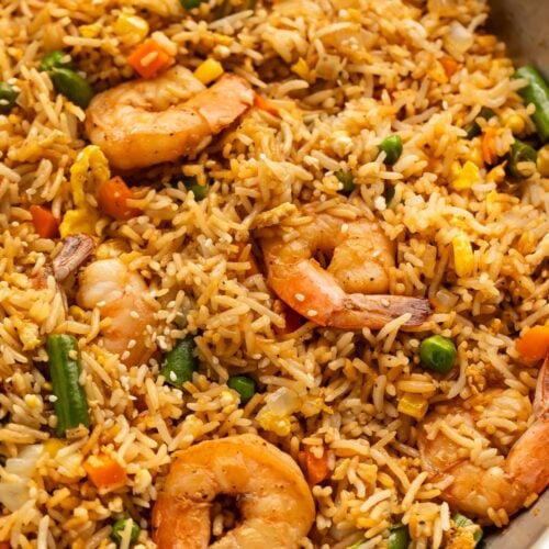 A large silver skillet holding fully-prepared shrimp fried rice with large juicy shrimp, green beans, and peas littered throughout.