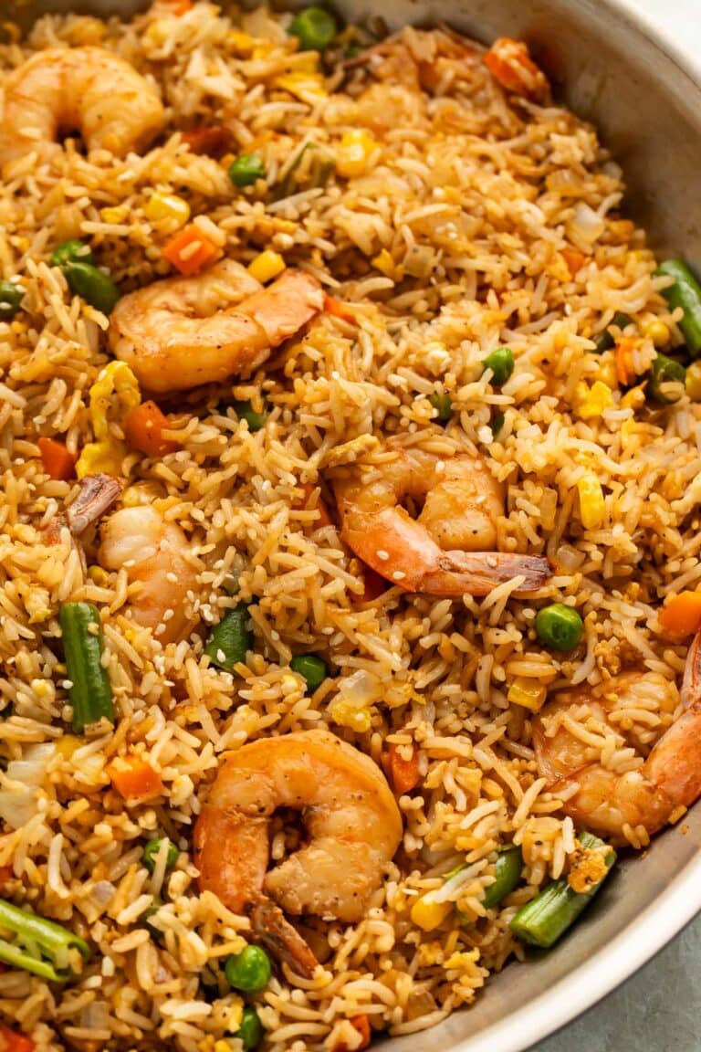 A large silver skillet holding fully-prepared shrimp fried rice with large juicy shrimp, green beans, and peas littered throughout.