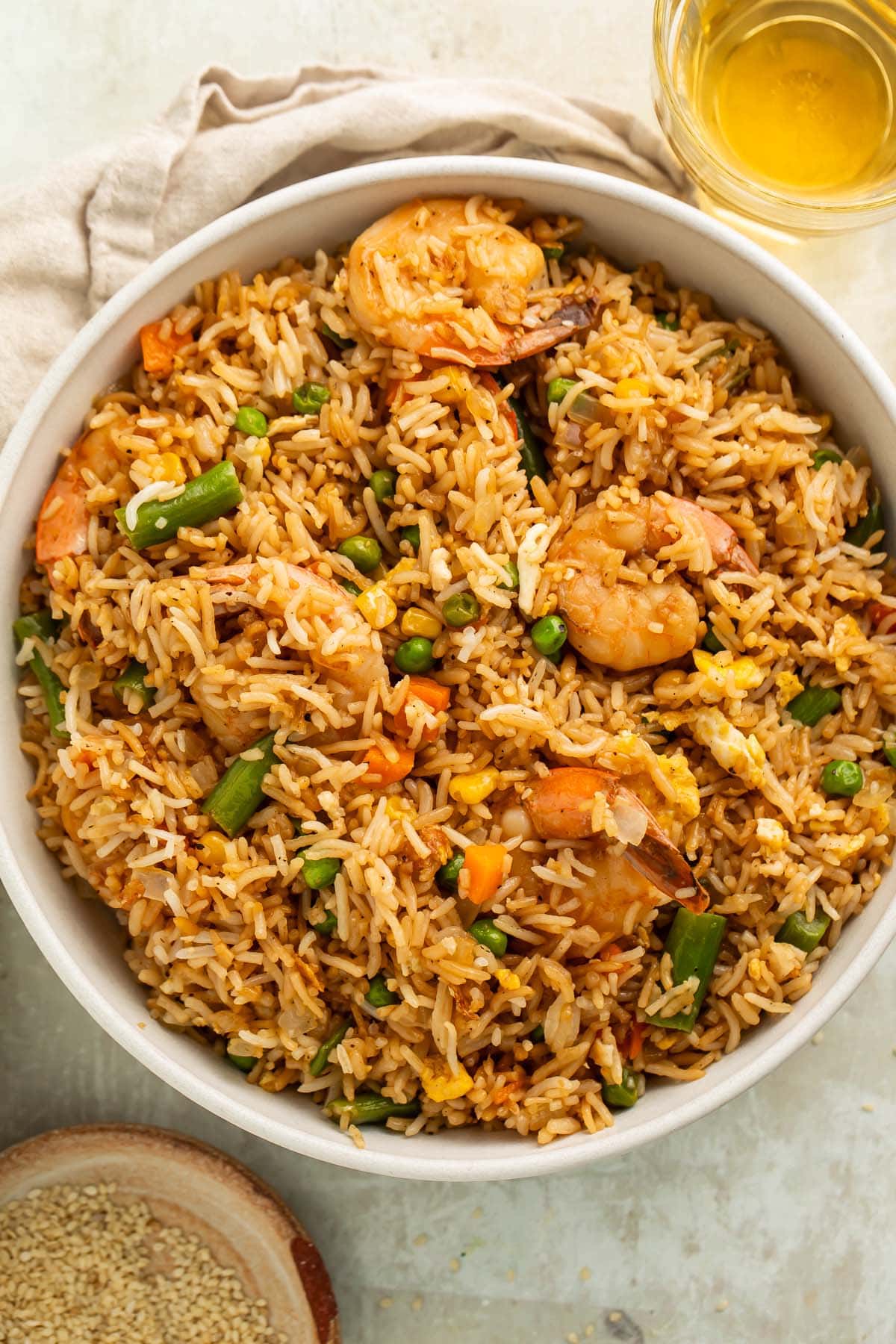 A large white bowl holding fully-prepared shrimp fried rice with large juicy shrimp, green beans, and peas littered throughout.