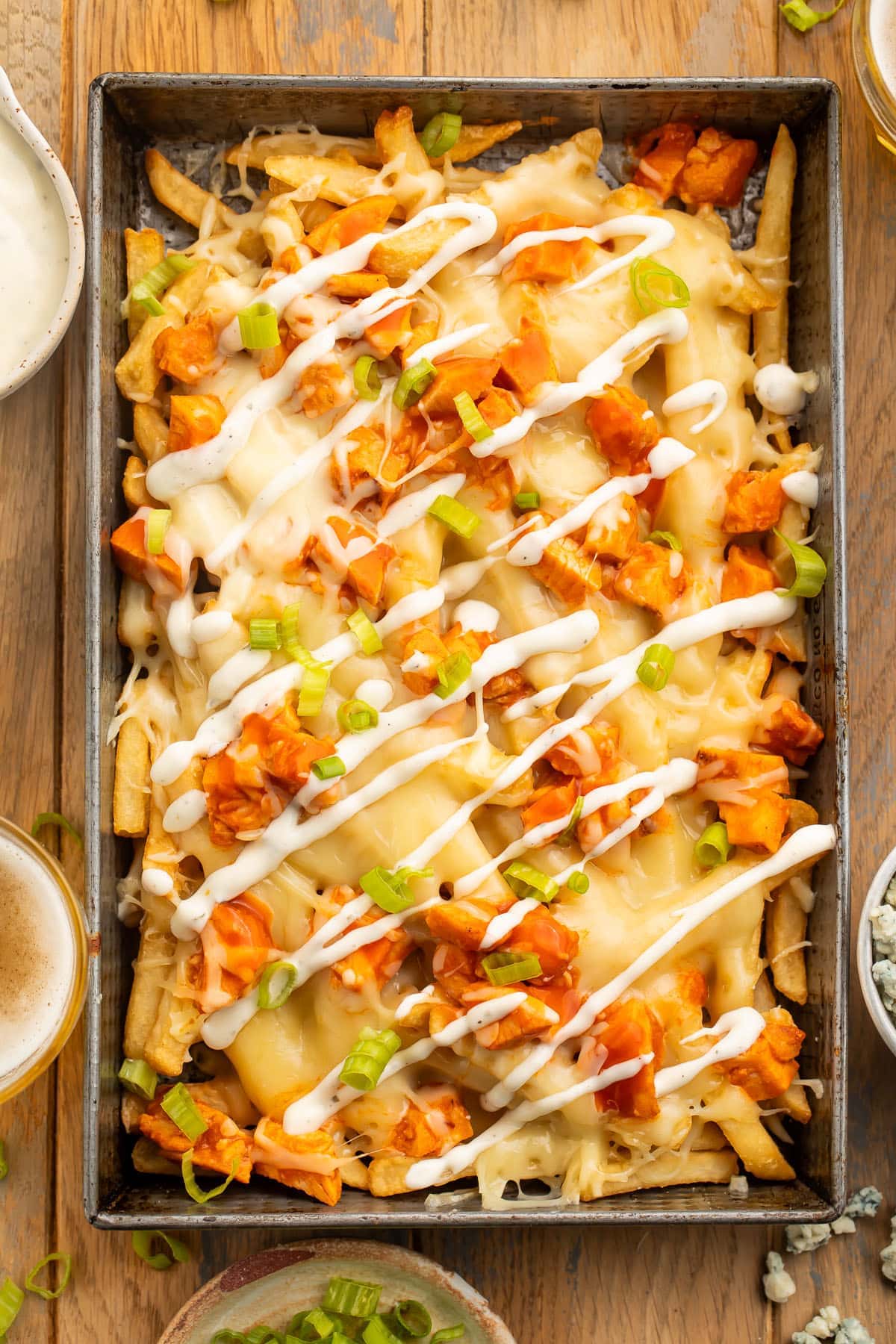 A large pan of fries topped with buffalo chicken, green onions, and ranch dressing.