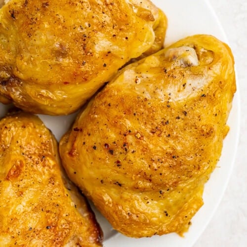 Fully cooked Instant Pot frozen chicken thighs on a round white plate.