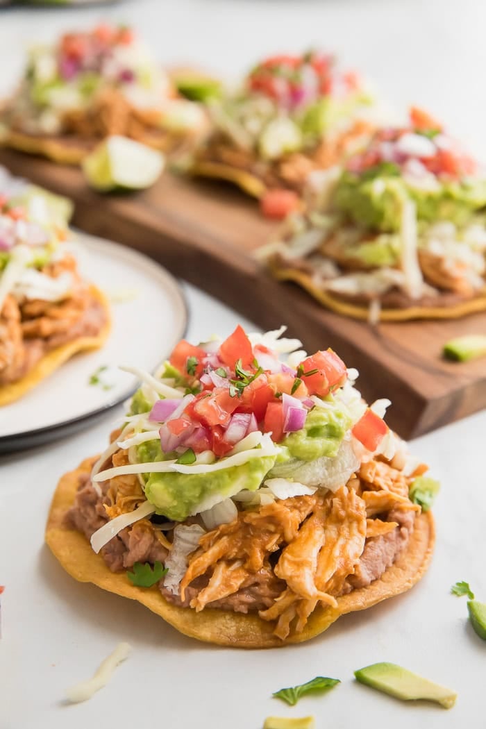 Healthy chicken tostadas on a plate in front of a pan of tostadas.